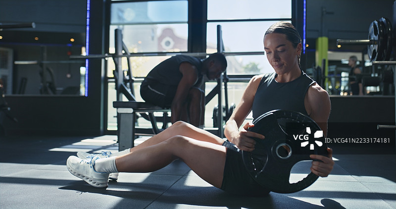 女性在健身房进行斜扭转和举重训练，注重地面平衡和核心力量锻炼。健美运动员与器械一起锻炼，挑战肌肉增长，专注于腹部训练。图片素材