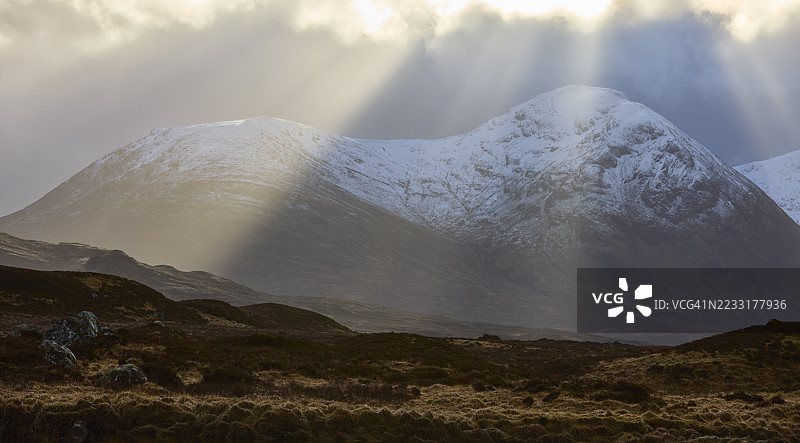 阳光透过乌云洒在苏格兰格伦科雪山上图片素材