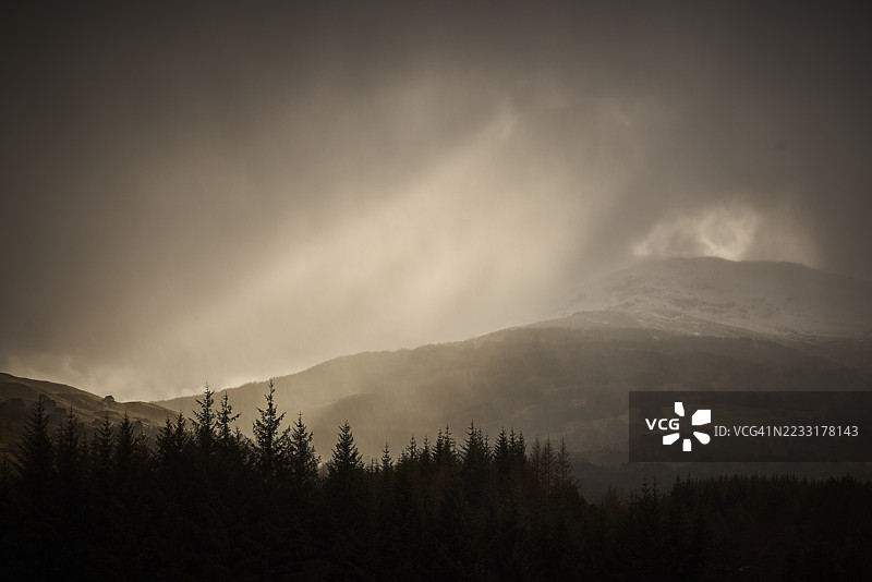 阳光透过乌云洒在树木和山脉上，格伦科，苏格兰，英国图片素材