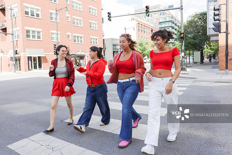 一群不同种族背景的年轻女性穿着休闲服饰，兴高采烈地走在城市街道上。图片素材