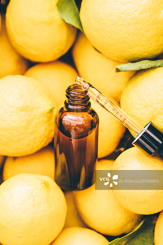 琥珀色滴管玻璃瓶中的柠檬精油提取物，旁边放着新鲜的柠檬。图片素材