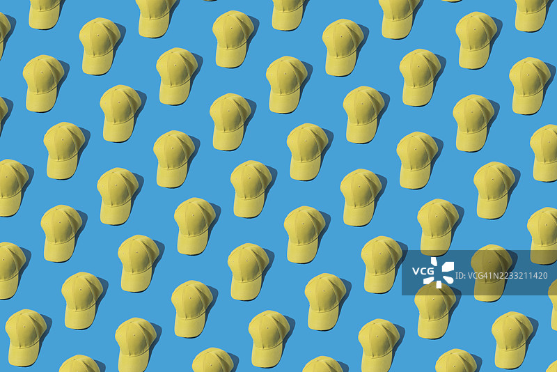 蓝色背景上的黄色棒球帽图案。时尚、服装、配饰、嘻哈、棒球、运动、制服和防晒。图片素材