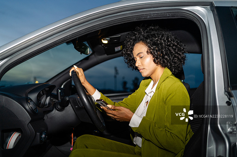 年轻女商人在夜间开车时用手机发短信，这是一种危险且违法的行为图片素材