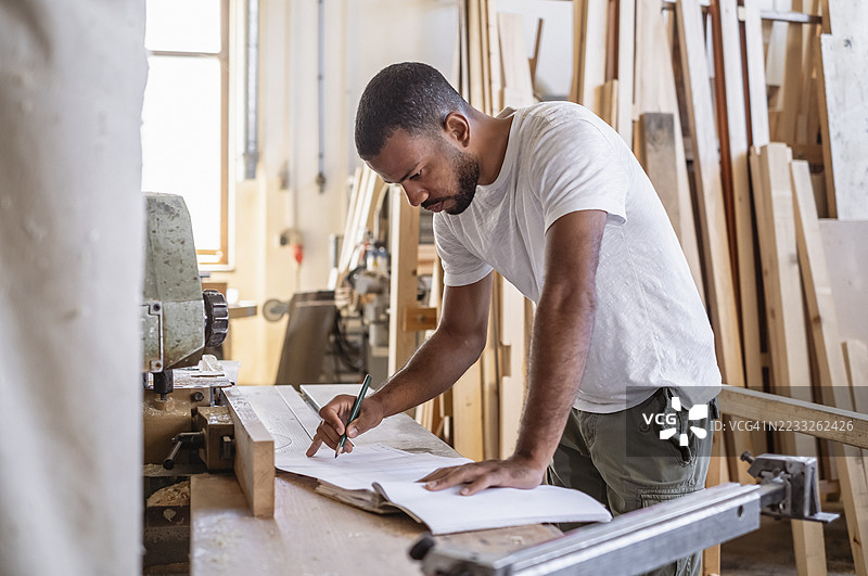 专注的多种族男性木匠穿着白色T恤在明亮的工作坊中工作图片素材