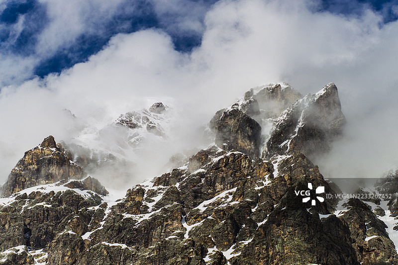 阳光明媚的日子里，雪覆盖的山峰穿透浓密的云层。图片素材