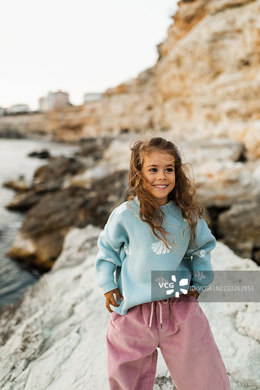 穿着时尚休闲服装的微笑儿童在岩石海岸户外玩耍图片素材