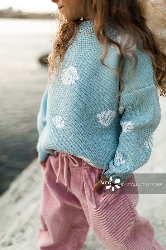 穿着舒适蓝色毛衣和粉色裤子的孩子在水边户外玩耍图片素材