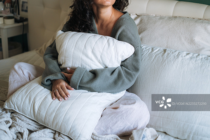 年轻女性在家中床上休息，怀抱枕头，享受舒适的早晨。图片素材