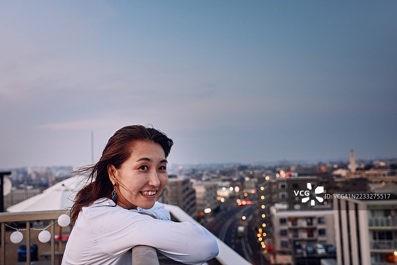 一位女性在建筑屋顶上凝视远方，背景是遥远的城市灯光。图片素材