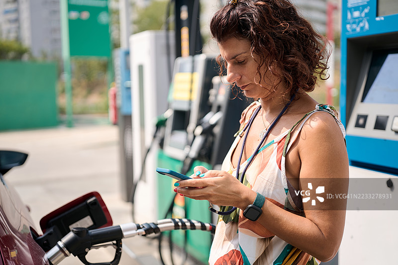 女性在加油站加油时使用智能手机图片素材