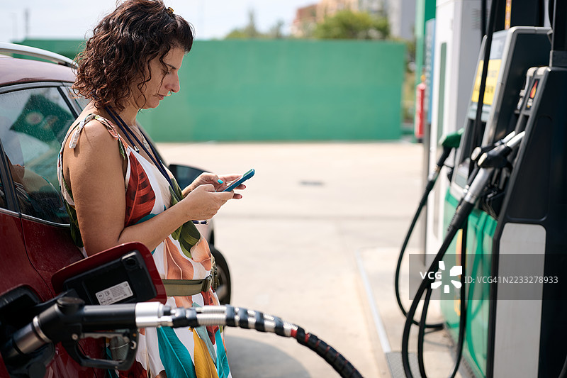 女人在加油站给汽车加油时使用智能手机图片素材