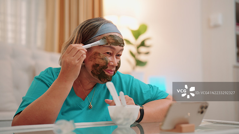 一位年长的亚洲女性正在用刷子将护肤面膜涂抹在脸上图片素材