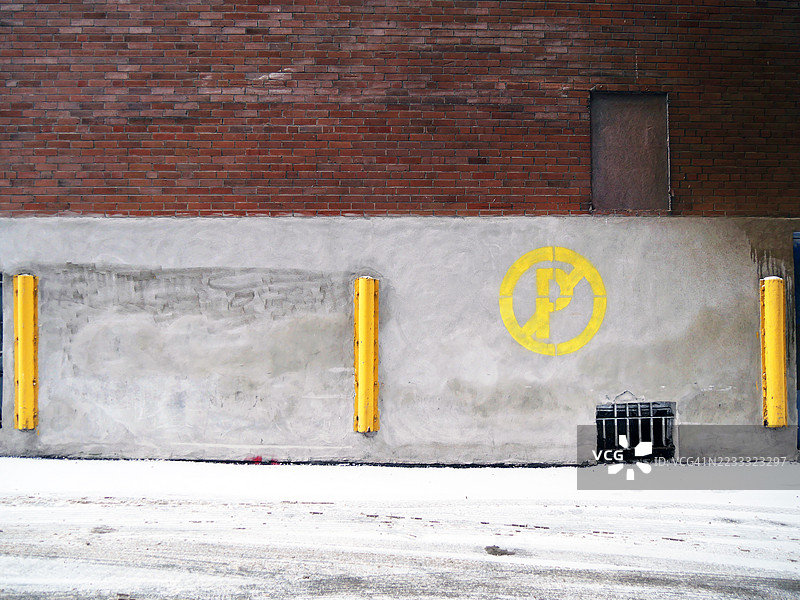 蒙特利尔，魁北克，加拿大。阳光下的雪地街道，锈迹斑斑的混凝土和砖墙上有一个禁止停车的标志。自然色彩。图片素材