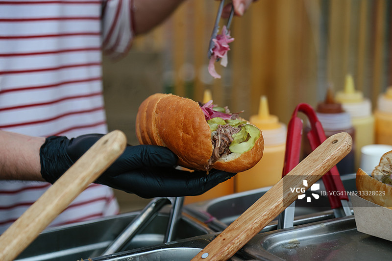 厨师的手在户外小吃摊为热狗添加额外的腌制红洋葱图片素材
