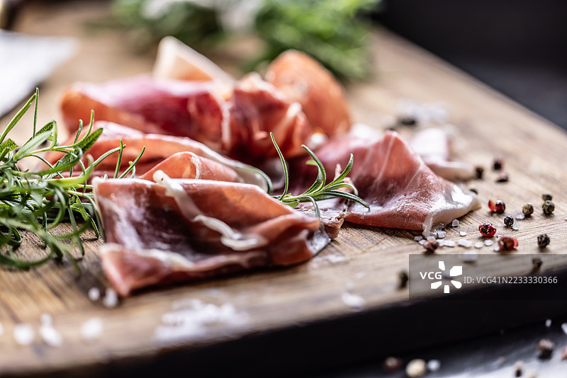 切片的塞拉诺火腿或帕尔马生火腿放在木板上，旁边有迷迭香。图片素材