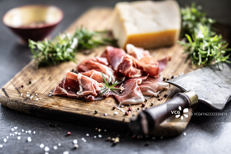 切片的塞拉诺火腿或帕尔马生火腿和帕尔马干酪，搭配迷迭香，摆放在木板上。图片素材