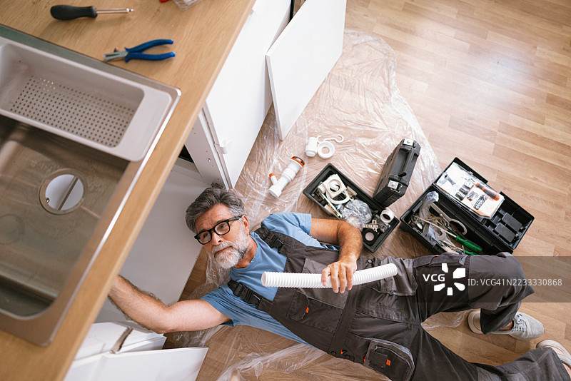 老年维修工在家中修理厨房水槽图片素材