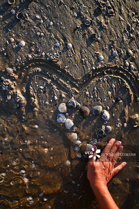 女人在海滩上用贝壳画心形图案图片素材