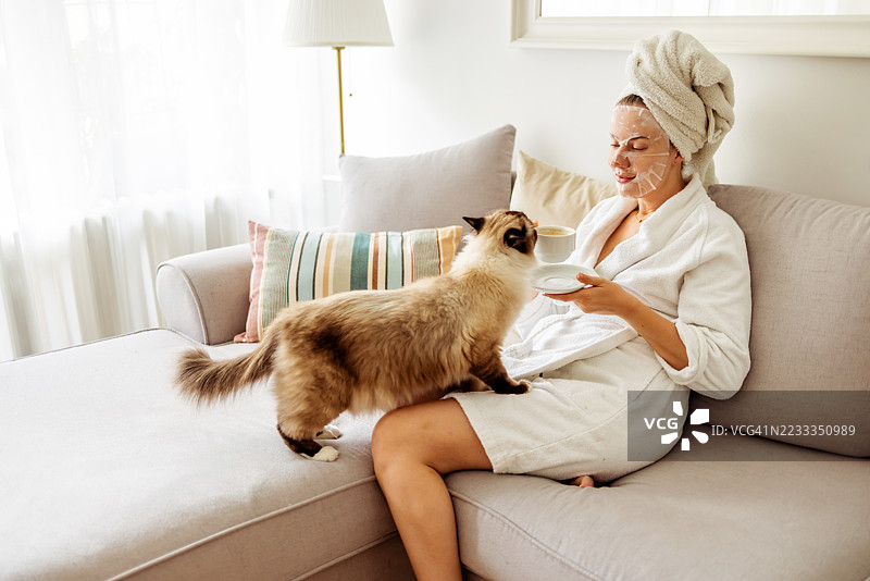 女人在家中享受与猫咪的放松时光，同时进行护肤。图片素材
