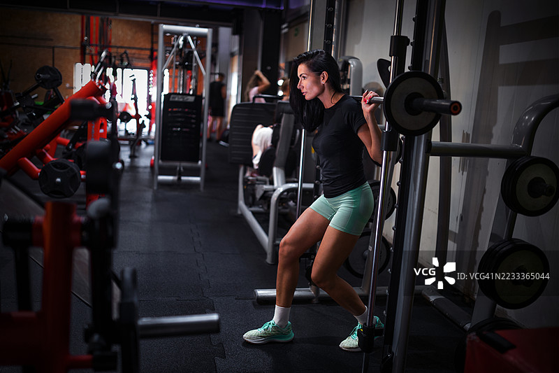 年轻女性在健身房使用史密斯机做深蹲图片素材