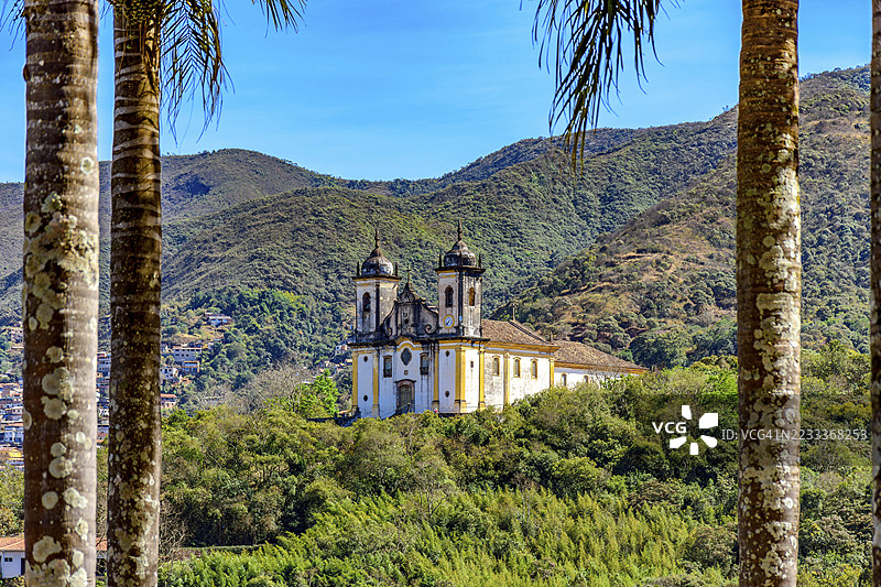 通过树木看到的历史巴洛克教堂的山丘，背景是巴西米纳斯吉拉斯州奥鲁普雷图市的山脉。图片素材