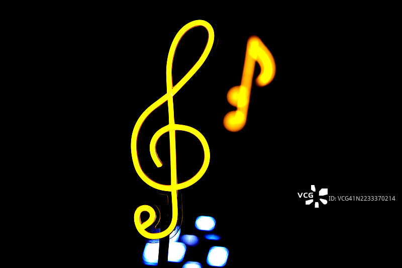 一个明亮的黄色高音谱号和一个单一的音符在黑色背景下发光，象征着音乐的普遍语言。图片素材