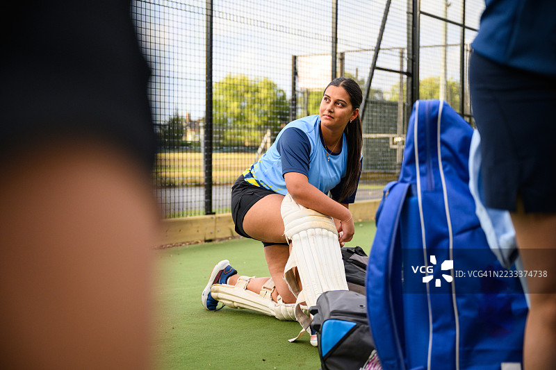 年轻女性在练习场的网中穿上保护垫，准备打击板球。图片素材