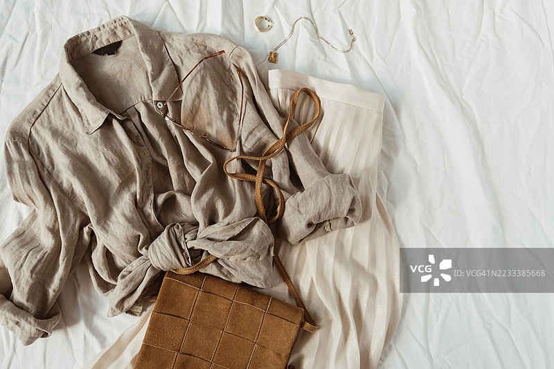 米色服装和配饰整齐地摆放在白色床上图片素材