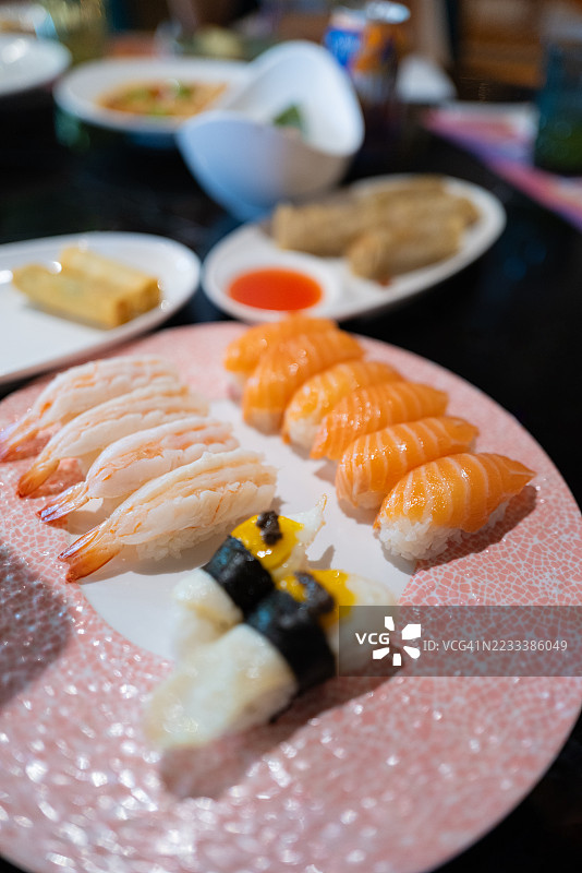 美味的寿司拼盘放在粉色盘子上，旁边还有其他菜肴图片素材
