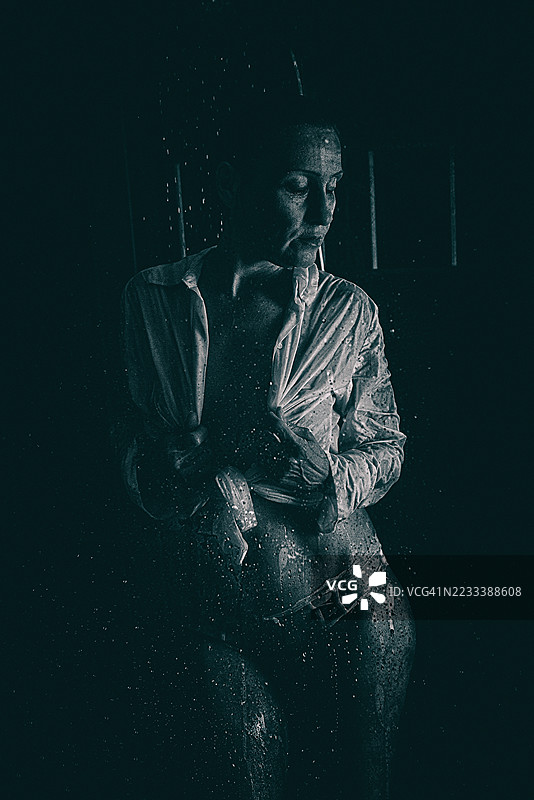 身着湿透衬衫的女子手持利剑，置身于戏剧化的光影之中图片素材