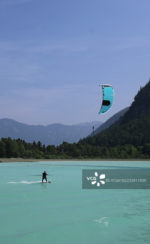 在群山环绕的碧绿湖面上滑行的风筝冲浪者图片素材