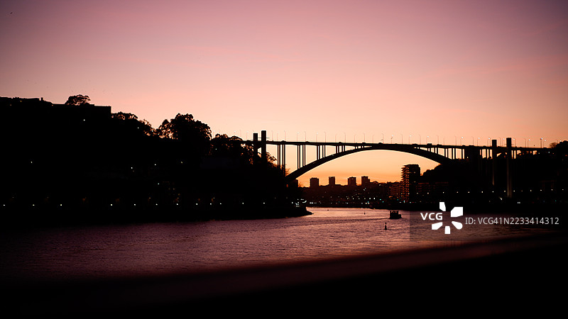 日落时分，葡萄牙波尔图一座桥的轮廓映衬在河面上图片素材