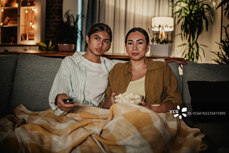 母女俩在家里享受温馨的夜晚，一边看电影一边分享爆米花。图片素材