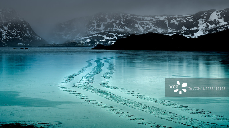 宁静的冰冻湖泊与雪山在阴云密布的天空下，挪威图片素材