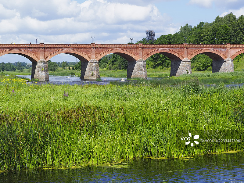 拉脱维亚郁郁葱葱的风景中的历史拱桥横跨河流图片素材