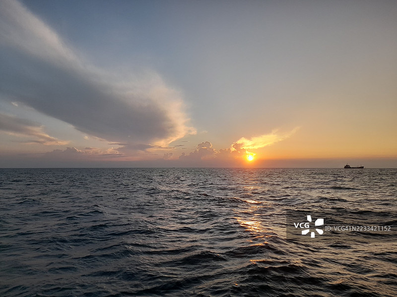 宁静的海洋日落与远处的船只，印度尼西亚沃诺萨里区图片素材