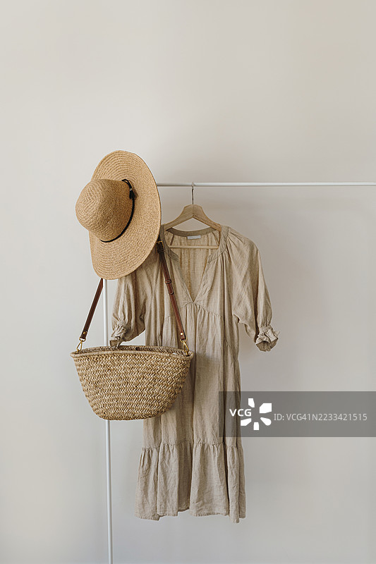 米色连衣裙和草帽挂在白色墙壁上的衣架上图片素材