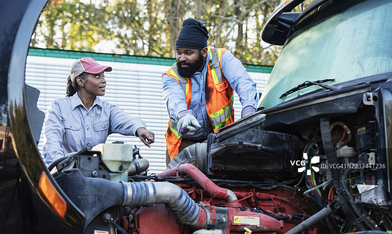 两名机械师正在检查一辆半挂卡车的引擎盖下。图片素材