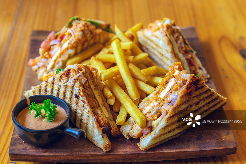 美味的烤三明治配薯条和酱汁，摆放在木板上图片素材