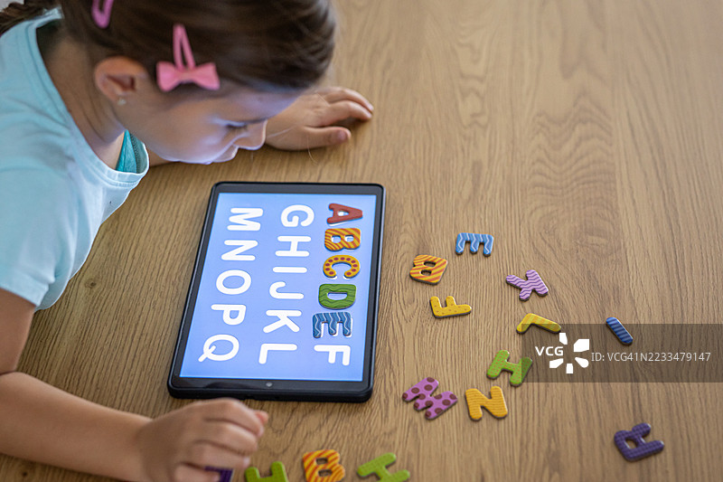 小女孩在室内使用平板电脑和五彩斑斓的智能字母学习字母表图片素材