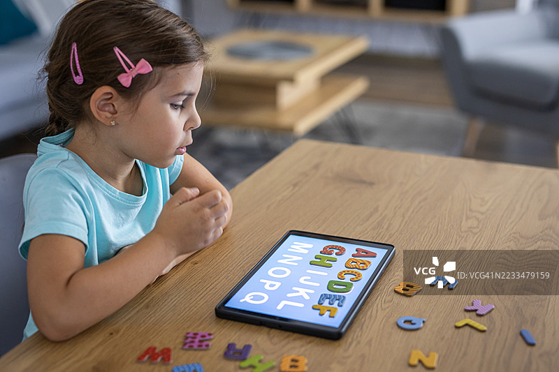 专注于字母学习活动的学前女孩与现代科技图片素材