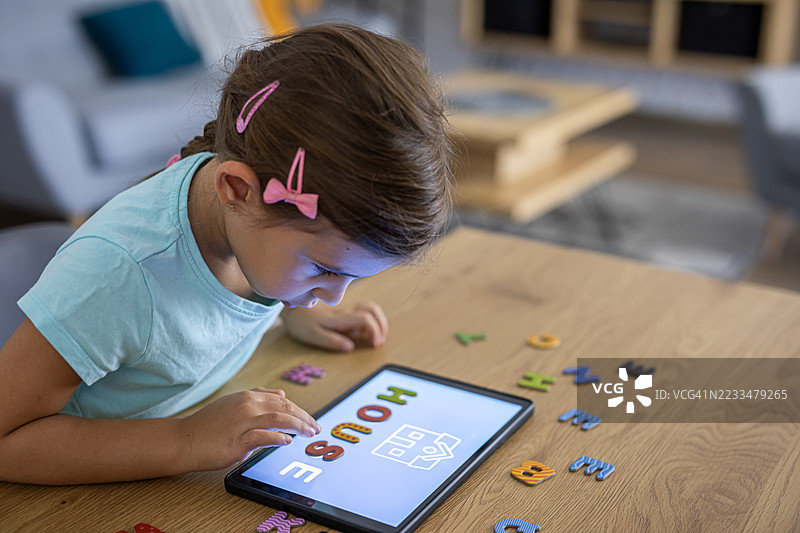 专注于字母学习活动的学前女孩与现代科技图片素材