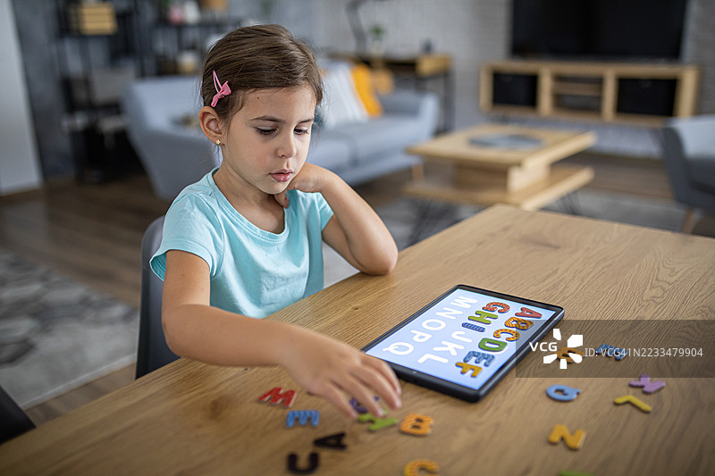 学龄前女孩专注于使用现代科技进行字母学习活动图片素材