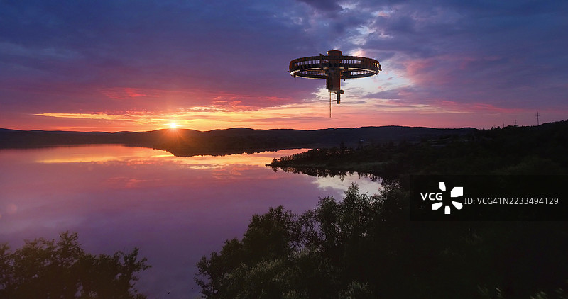 一艘科幻飞船漂浮在宁静的湖面上方，紫色和橙色的傍晚天空中。图片素材