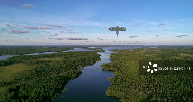 一艘大型宇宙飞船悬停在宽阔的河流和茂密的绿色森林上方，蓝天明亮。图片素材