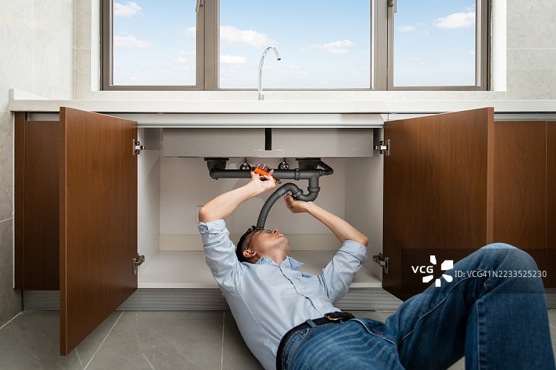 男子在厨房水槽下修理管道图片素材