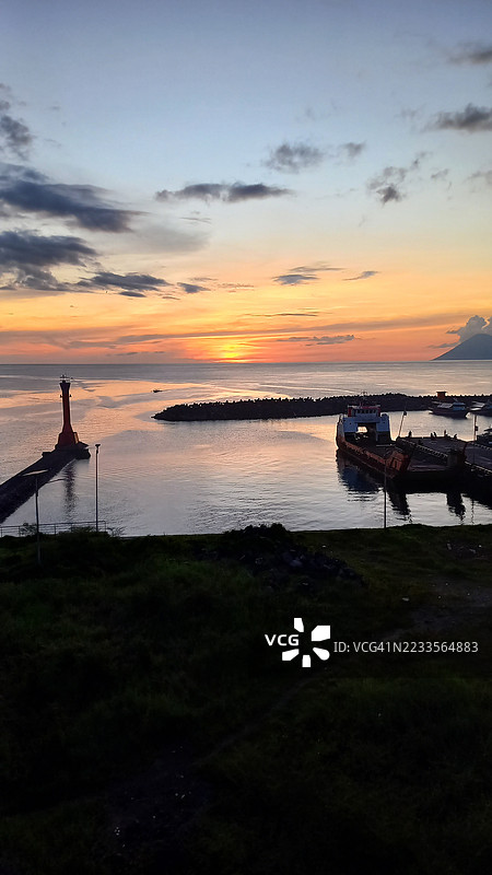 宁静海面上的日落，灯塔和码头相映成趣图片素材