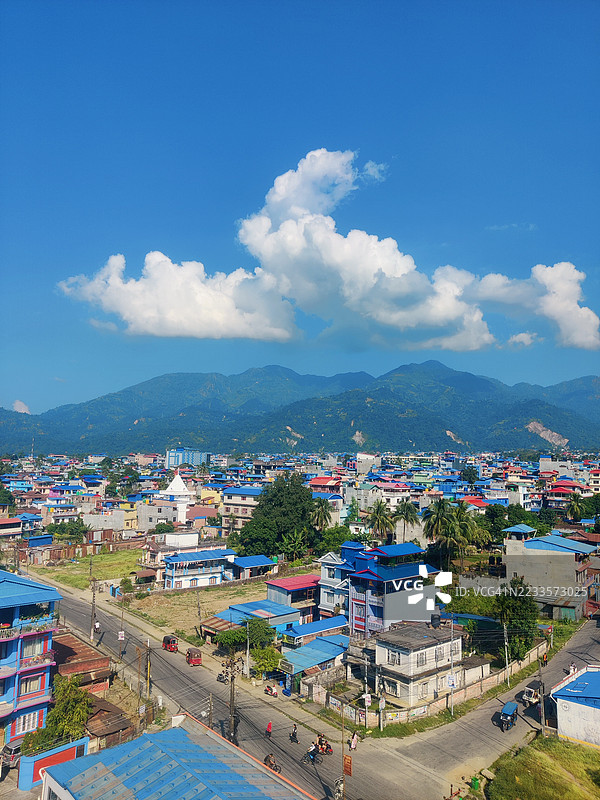 宁巴尔，尼泊尔，蓝色屋顶和山脉下的生机勃勃的城镇全景，晴朗的天空。图片素材