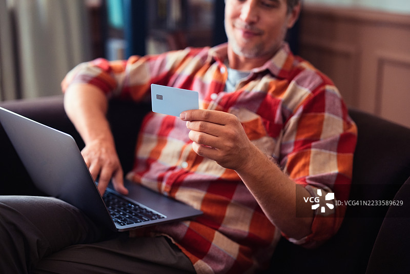男子在轻松的环境中使用笔记本电脑和信用卡进行在线购物图片素材
