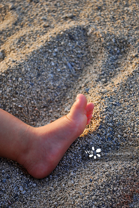 一个孩子的脚轻轻地 resting 在柔软的沙子上特写镜头。图片素材